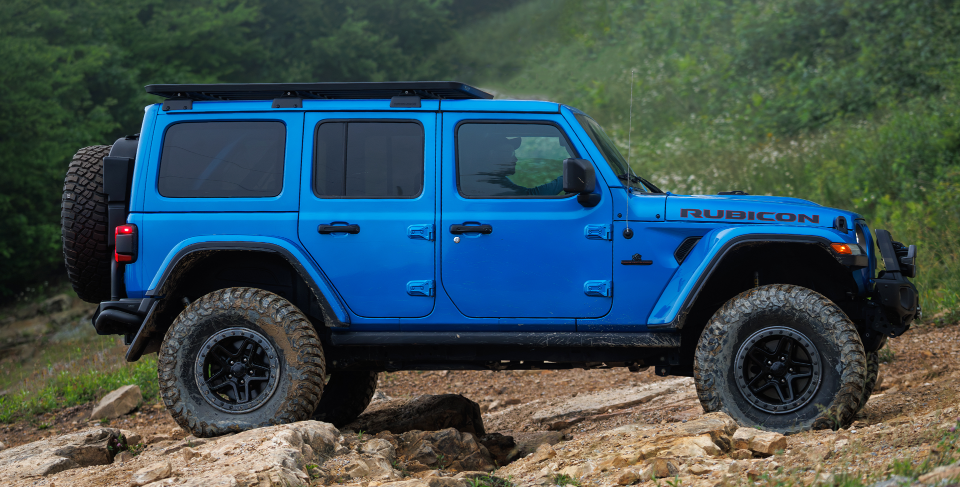 Blue Jeep Wrangler on a rocky trail with greenery in the background | Shown with 37" BFGoodrich KM3 tires